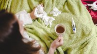 Woman with cold in bed with tissues and thermometer