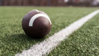 American football ball on green grass field background.